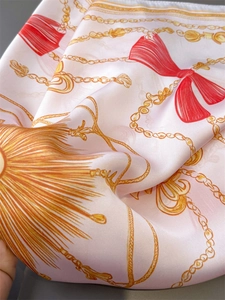 Detailed macro view of silky pink scarf with golden chains and red bow print pattern