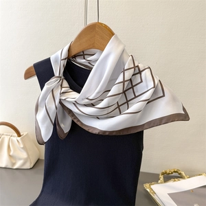 Detail of a white silk scarf with brown geometric grid patterns tied on a black neck top
