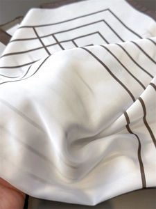 Detail shot showing the silky texture and brown linear pattern of the white square scarf