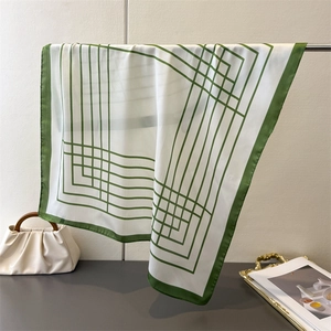 Close-up of a silk-feel square scarf with green geometric lines and elegant drape