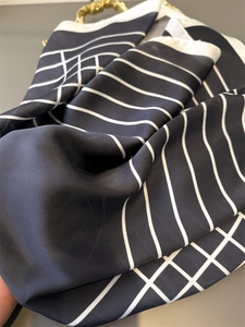 Close-up of black silk scarf with white linear patterns and gold metal chain detail