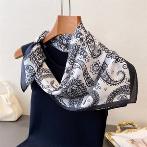 Detail of silk-like paisley pattern scarf draped over a black vest with pearl handbag