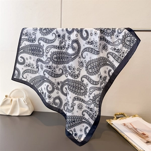 Elegant white paisley silk scarf with black borders hanging on a minimal display stand