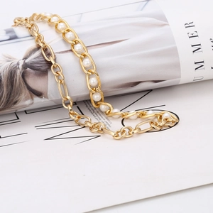 Collier chaîne dorée et perles blanches sur fond blanc avec décor de magazine