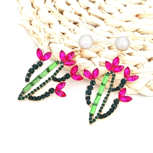 Exaggerated cactus earrings with colorful rhinestones and white pearls on a woven mat
