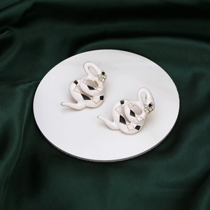 Minimalist snake earrings with white enamel and sparkling crystals on green silk fabric