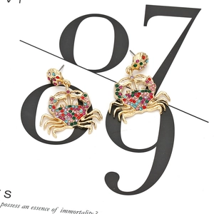 Boucles d'oreilles crabe dorées avec strass colorés et clous en coquillage sur fond blanc