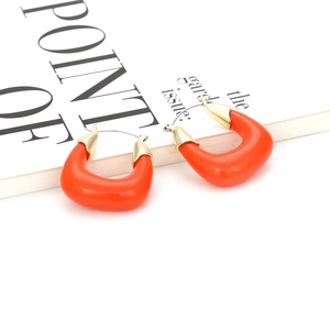 Détail de boucles d'oreilles créoles orange en résine en U avec tiges dorées sur magazine