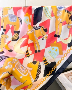 Detailed view of silk square scarf featuring cartoon horse and gold chain patterns