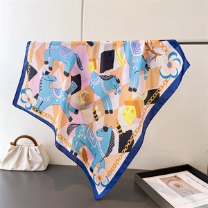 Blue horse print silk scarf draped over a metal rod with a stylish white handbag
