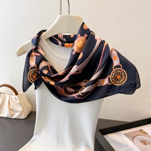 Detail of navy blue silk scarf with gold chain print draped on a white vest and hanger