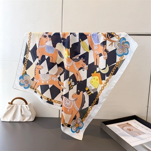 Close-up of silk-like square scarf featuring horse prints and golden chain borders
