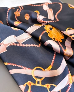 Macro detail of silk scarf featuring golden chain and pink ribbon print on navy blue fabric