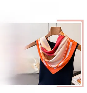 Détail d'un foulard en soie avec imprimé équestre et bordure orange sur un cintre
