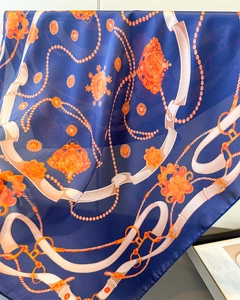 Close-up of navy blue silk-feel scarf with vintage orange chain and buckle print