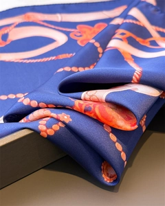 Macro detail of silk scarf with luxury chain prints and satin texture on a dark background