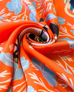 Macro shot of silk scarf fabric showing orange floral patterns and glossy draped texture