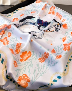 Detailed view of square silk scarf with orange floral and horse prints on satin fabric