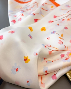 Detailed macro view of ivory silk-like scarf with colorful floral patterns and orange hem