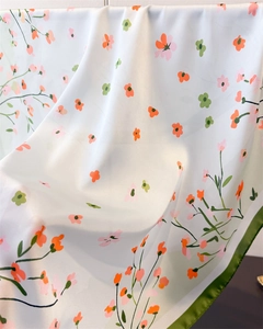 Detailed view of silky floral scarf featuring orange prints and green rolled edges