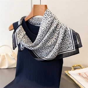 Detail of leopard print silk scarf styled on a navy vest with luxury accessories