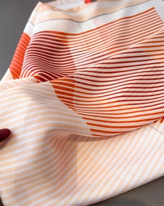 Close-up of geometric striped silk scarf featuring orange and red modern patterns