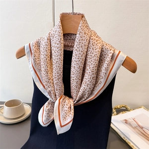 Leopard print satin square silk scarf with contrast orange border hung on a wooden hanger