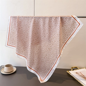 Detail of leopard print silk scarf showing smooth texture and orange border on a metal rack