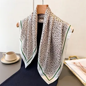 Leopard print silk-like square scarf with dark green borders draped on a hanger
