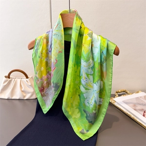 Carré en soie verte avec motif floral de lys suspendu sur un cintre en bois