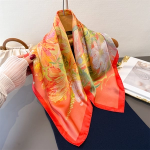 Vibrant floral silk scarf with red edges hung on a hanger in a stylish setting