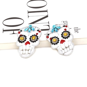 Orecchini a teschio fatti a mano con strass colorati e perle bianche su sfondo di una rivista