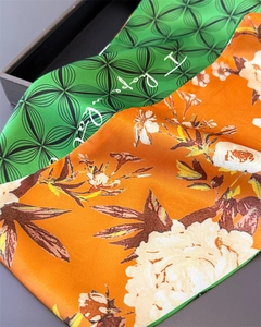 Detail of premium satin silk scarves featuring green geometric and orange floral prints