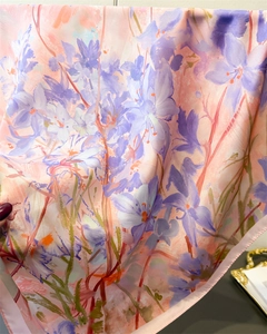 Dettaglio macro di un foulard di seta pesca con stampe floreali e bordi arrotolati