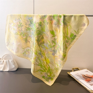 Dettaglio di un foulard in seta a fiori drappeggiato vicino a una borsa con manico di perle