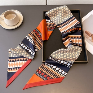 Flat lay of an elegant long silk scarf with orange and navy geometric patterns and tassels