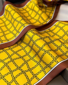 Gros plan d'un foulard en soie jaune avec grille géométrique noire et bords marron