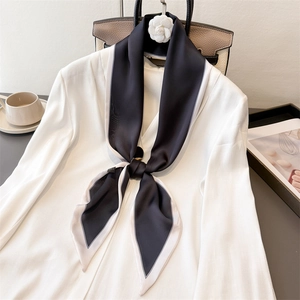 Detail of a minimalist black silk scarf with white piping styled on a white blazer