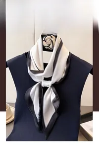 Detail of a minimalist silk-like scarf with black edges and a classic camellia brooch