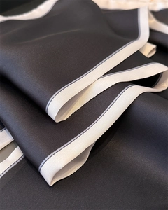 Detail showing the smooth silk texture and elegant white piping on the black neck scarf