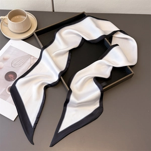 Elegant white silk-feel skinny scarf with black trim folded on a modern tray