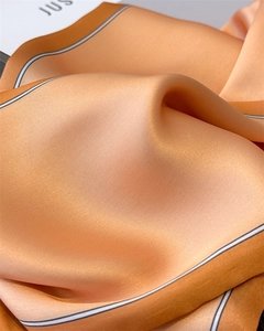 Detailed close-up of apricot silk scarf featuring elegant grey striped edge and satin texture