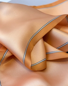 Detail of smooth apricot silk scarf texture with elegant black and white striped edges