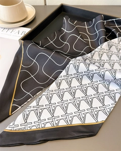 Detail of elegant black and white geometric silk scarf with gold edges on a tray