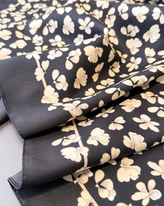 Nahaufnahme eines schwarzen Seidenschals mit beigen Blumenmustern und feiner Köperstruktur