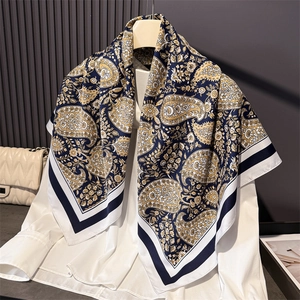 Elegant paisley silk-like square scarf in navy blue and gold draped on a wall display