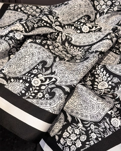 Macro detail of black and white paisley silk scarf with refined striped edge