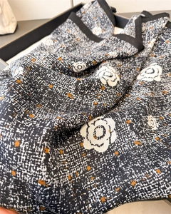 Détail d'un foulard en soie avec imprimé camélia et texture à chevrons sur tissu noir et blanc
