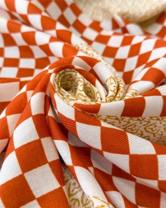 Détail d'un foulard en soie orange à carreaux avec motifs floraux dorés et tissage sergé