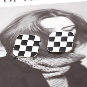 Boucles d'oreilles carrées en émail à motif damier posées sur un magazine de mode